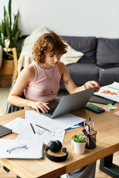 Young woman with curly hair immersed in work at her laptop surrounded by sketches and plants