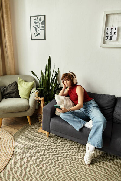 Curly-haired woman lounges on a couch, immersed in her phone while unwinding in her apartment.