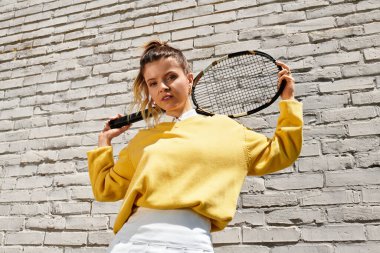 Genç ve güzel bir kadın, yaz ruhunu sergileyerek, tenis raketiyle rahatça poz veriyor..