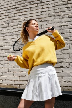 Genç ve güzel bir kadın, yaz eğlencesi için giyinirken tenis raketiyle yeteneklerini sergiliyor..