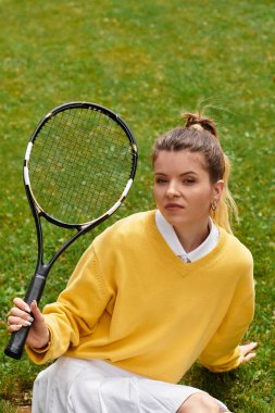 Parlayan yaz titreşimleri, güzel genç bir kadın yeşil çimlerde tenis raketiyle poz veriyor..