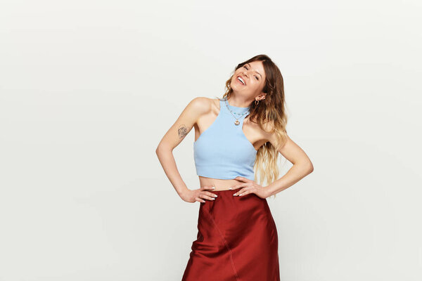 A young woman exudes confidence in a light blue top and flowing skirt, smiling brightly.