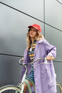 Parlak yaz kıyafetleri içinde neşeli genç bir kadın modern binaların önünden bisikletini sürüyor..