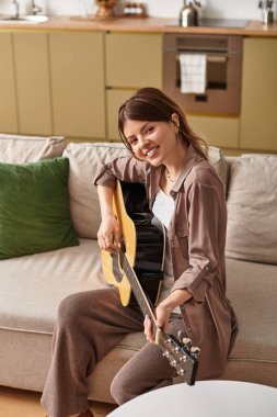 Gülümseyen kadın gelişigüzel giyinmiş gitarını parlak, havadar, dekorla dolu bir mekanda çalıyor..