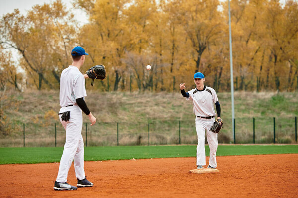 Два подростка практикуют бейсбольные навыки на ярком поле в окружении красочных осенних деревьев.