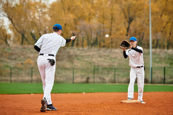 Два молодых бейсболиста тренируются бросать и ловить мяч на поле.