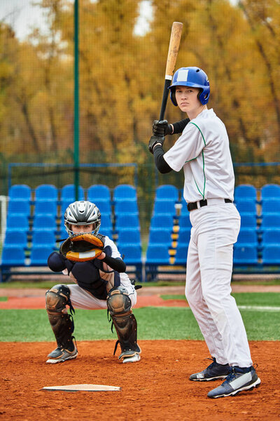 Two teenage boys play baseball on a vibrant field surrounded by autumn foliage.
