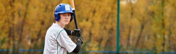 A young athlete stands ready at bat, focused on the game ahead in an autumn setting, banner