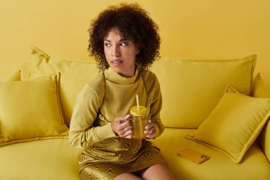 Sarı renklerle dolu parlak stüdyo, elinde içki tutan şık bir kadını yakalıyor..