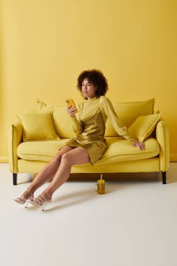 Parlak renkli stüdyoda sarı elbiseli kıvırcık bir kadın akıllı telefonuna odaklanmış ve dinleniyor..