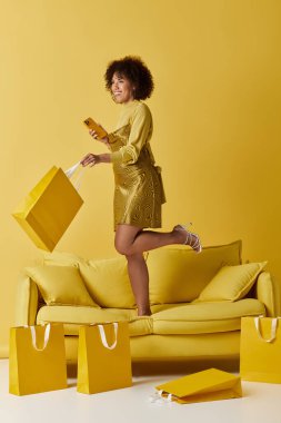 Kalın sarı elbiseli kıvırcık saçlı bir kadın alışveriş torbaları arasında akıllı bir telefonla neşe içinde meşgul oluyor..