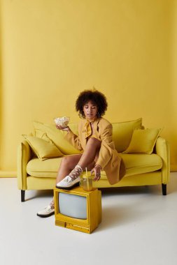 Parlak bir stüdyoda, kıvırcık saçlı bir kadın sarı kıyafetiyle patlamış mısırın tadını çıkarırken rahatlar..