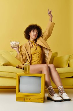 Sarı giysili kıvırcık kadın kendine güveniyor. Aydınlık bir ortamda atıştırmanın tadını çıkarıyor..