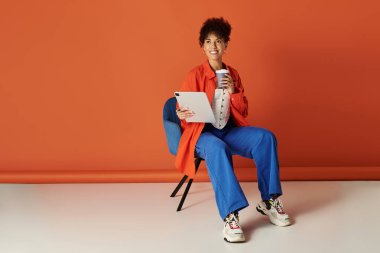 Parlak bir stüdyoda, kıvırcık Afrikalı Amerikalı bir kadın rahatça oturup tabletle meşgul oluyor..