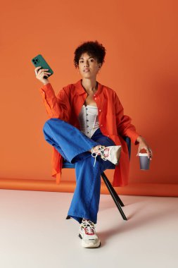 Canlı bir stüdyoda şık bir kadın akıllı telefonunu tutarken modasını sergiliyor.