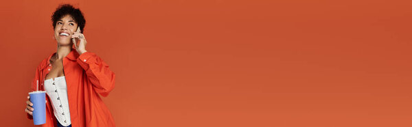 Curly-haired woman in vibrant outfit engages with her smartphone in a lively studio setting, banner