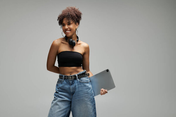 Стильная женщина уверенно стоит, держа планшет в шикарном наряде.