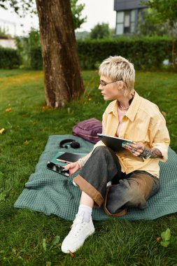 Tarz sahibi genç bir kadın yeşil bir ortamda defteriyle çimlerin üzerinde rahatlar..