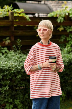 Çizgili tişörtlü genç bir kadın parkın huzurunu kucaklıyor, kahvesini yudumluyor..