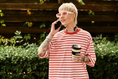 Çizgili tişörtlü güzel bir kadın telefonuyla sohbet ediyor, elinde içki var..