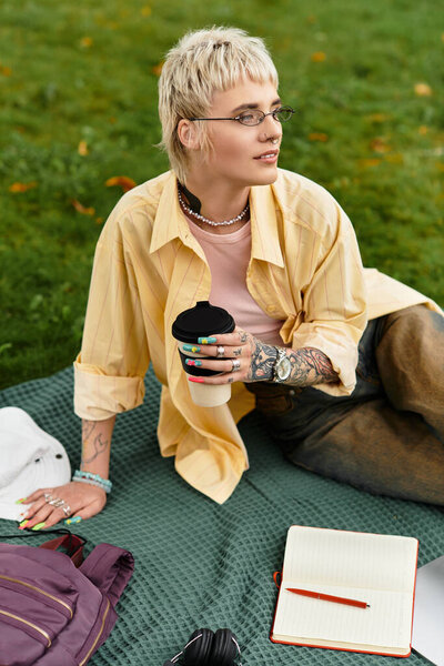 Relaxing in the park, a young woman sips coffee while reflecting in her notebook.