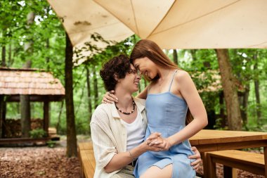 Genç bir çift ağaçların gölgesinde dinlenirken neşeli ve samimi bir anı paylaşır..