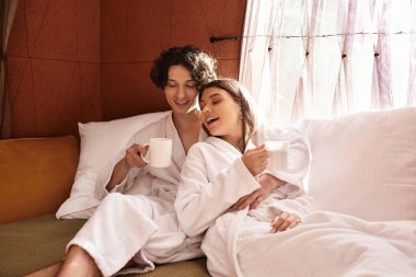 Sıcak içecekleri ve kahkahaları paylaşırken sevimli çift rahat bir kanepede sarılır..