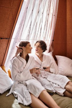 Çift rahat bir yatakta oturuyor, içkilerini ve kahkahalarını evde paylaşıyor..