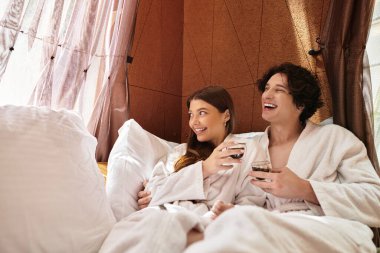 Yumuşak elbiselere bürünmüş genç bir çift rahatlama ortamında kahkaha ve içkileri paylaşıyor..