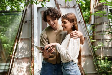 Genç çift, güneşli bir günde doğayla iç içe olan bir tabletle güler..