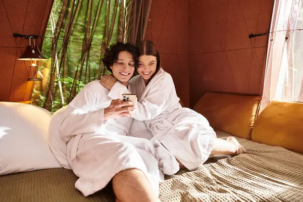 Bornozlu genç çift huzurlu bir ortamda telefona bakarken keyifli bir anı paylaşıyor..