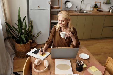 Üst düzey güzel kadın kahve içer ve mutfaktaki ahşap masada notlar alır..