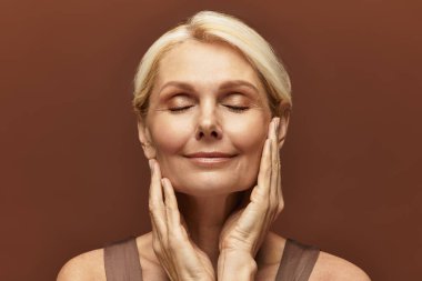 Mutlu bir gülümsemesi olan güzel bir son sınıf kadını yüzüne hafifçe dokunur, huzur ve güven saçar..