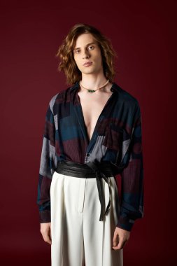 Genç bir adam, minimalist bir ortamda göze çarpan giysiler sergiliyor..