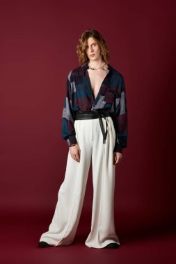 Genç, şık bir adam koyu kırmızı bir arka plana karşı poz verirken cesur bir moda ifadesi sergiliyor..