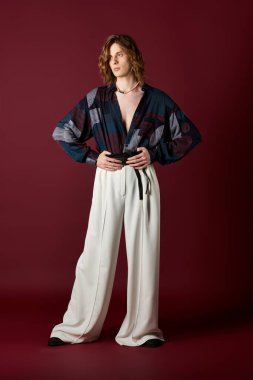 Genç yakışıklı bir adam eşsiz bir moda sergiliyor, zengin bir arkaplana karşı güvenle poz veriyor..