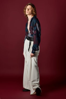 Şık bir genç adam, zengin bir bordo arka planına karşı özgüvenle poz verir..