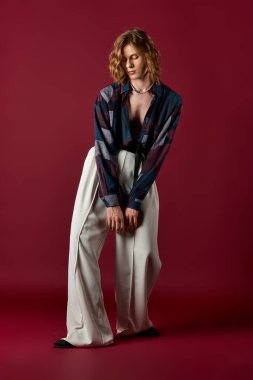 Şık bir genç adam, kendine güvenerek parlak kırmızı bir arka plana karşı moda anlayışını sergiliyor..