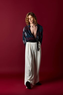 Genç bir adam kadınlığı ve stili harmanlıyor, cesur bir arkaplan karşısında kendine güven yayıyor..