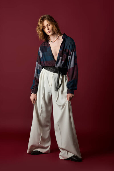 Красивый молодой человек демонстрирует стильный наряд со свободными брюками и яркой рубашкой.