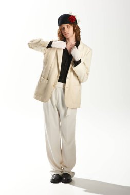 Genç adam modaya uygun giyinerek çekicilik sergiliyor. Minimalist bir arkaplanda zarifçe poz veriyor..