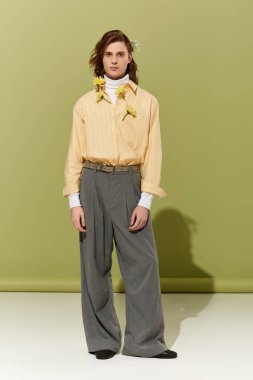 Büyük giyimli, genç, yakışıklı bir adam kendine güvenen, modaya uygun, kadınsı bir tarzda duruyor..