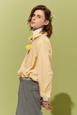 Genç bir adam, parlak yeşil bir arka planda çiçeklerle süslenmiş şık bir kıyafet sergiliyor..