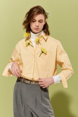 Genç bir adam pastel bir odada kendine güvenerek poz verir, şık bir şekilde çiçek katmanları giyer..