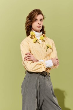 Kendine güvenen genç bir adam yumuşak yeşil bir arka planda çiçek aksanıyla tarzını sergiliyor..