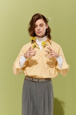 Çiçek gibi giyinmiş kendine güvenen genç adam yemyeşil bir zemin üzerinde duruyor..