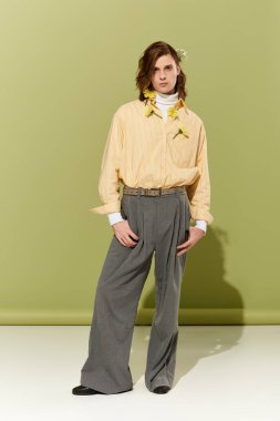 Genç bir adam kendine güveni olan şık bir elbiseyle poz veriyor. Çiçeklerle birlikte yeşil bir arka planda..