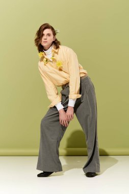 Genç, yakışıklı bir adam, canlı yeşil bir zemine karşı yumuşak pastel renkte şık bir kıyafet sergiliyor..