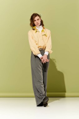 Kadınsı bir dokunuşu olan genç bir adam şık bir şekilde minimalist yeşil bir zemine karşı duruyor..