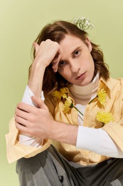 Yakışıklı genç bir adam özgün tarzını sergileyerek yumuşak yeşil bir zemine karşı düşünceli bir şekilde poz verir..